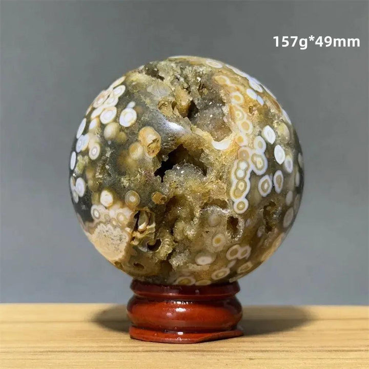 Ocean Jasper sphere from Crystal Destiny, with green, white, and brown orbicular patterns on a red wood base.
