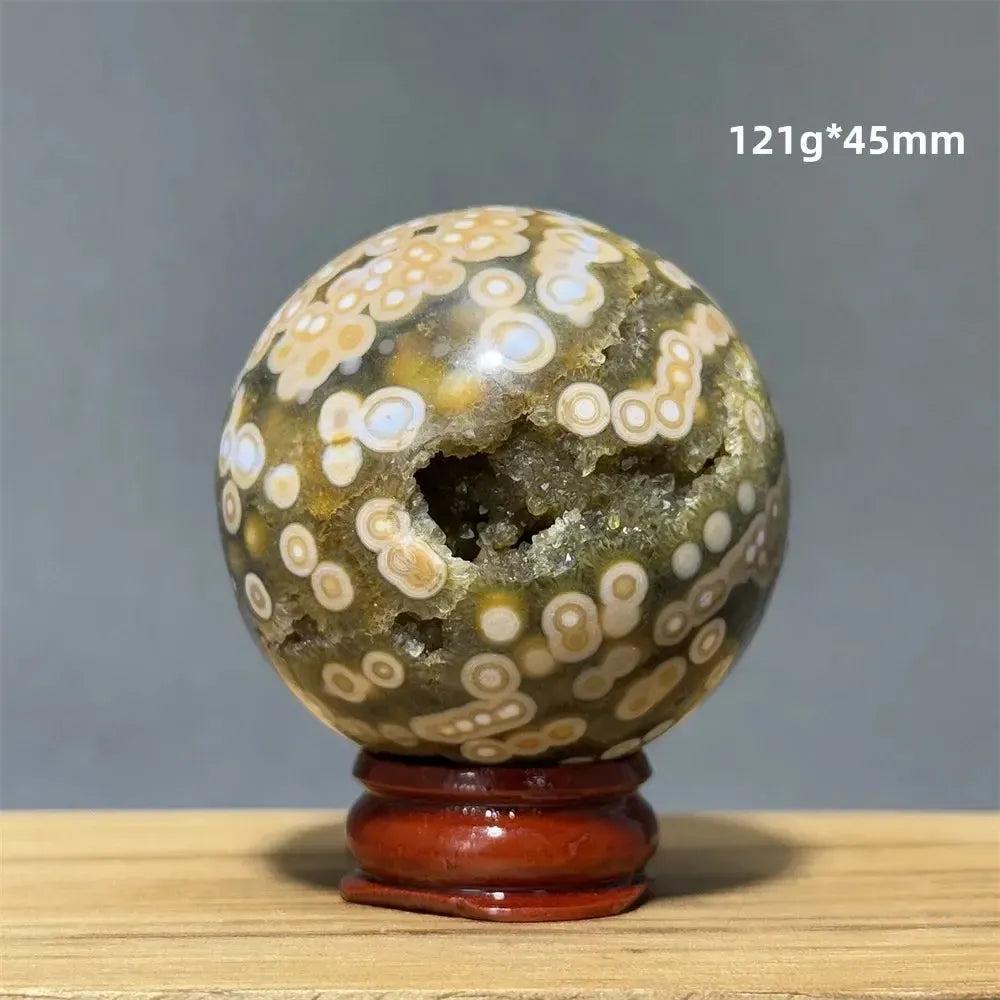 Ocean Jasper sphere with orbicular patterns in green, white, cream, pink, and red, on a wooden base.