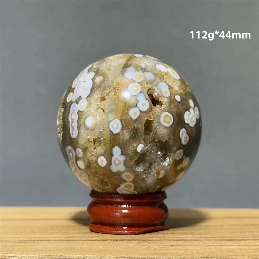 Ocean Jasper sphere from Crystal Destiny, with green, white, cream, pink, and red orbicular patterns on a wood base.