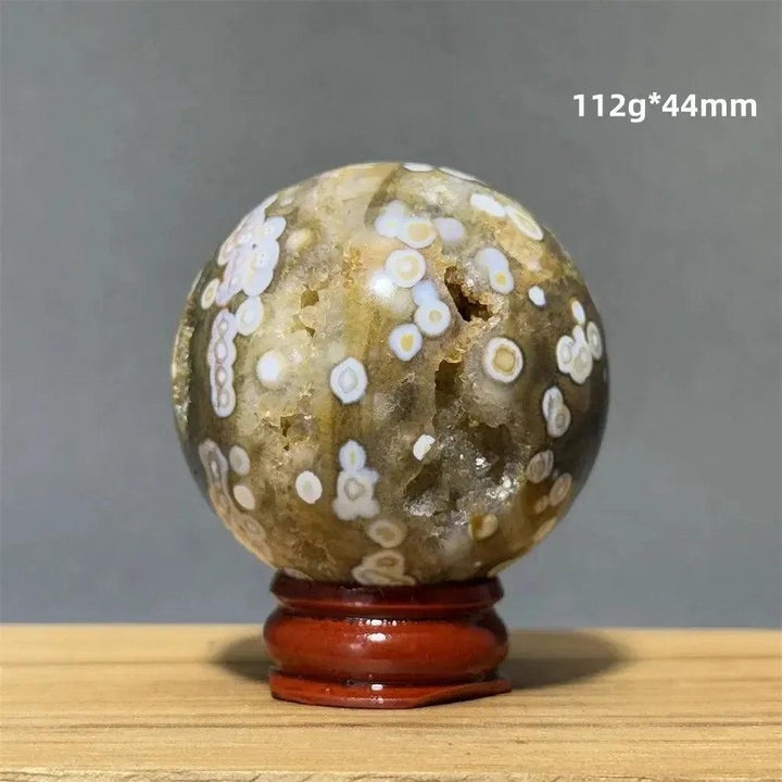 Ocean Jasper sphere from Crystal Destiny, with green, white, cream, pink, and red orbicular patterns on a wood base.