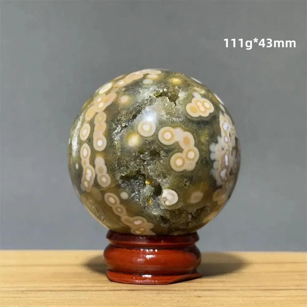 Ocean Jasper sphere from Crystal Destiny, 43mm, with green, white, cream, pink orbicular patterns on a wood base.
