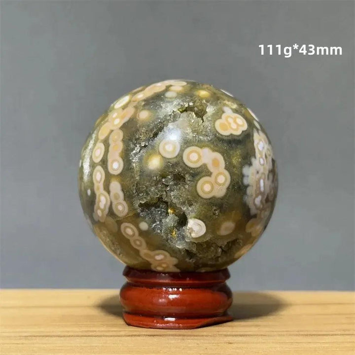 Ocean Jasper sphere from Crystal Destiny, 43mm, with green, white, cream, pink orbicular patterns on a wood base.