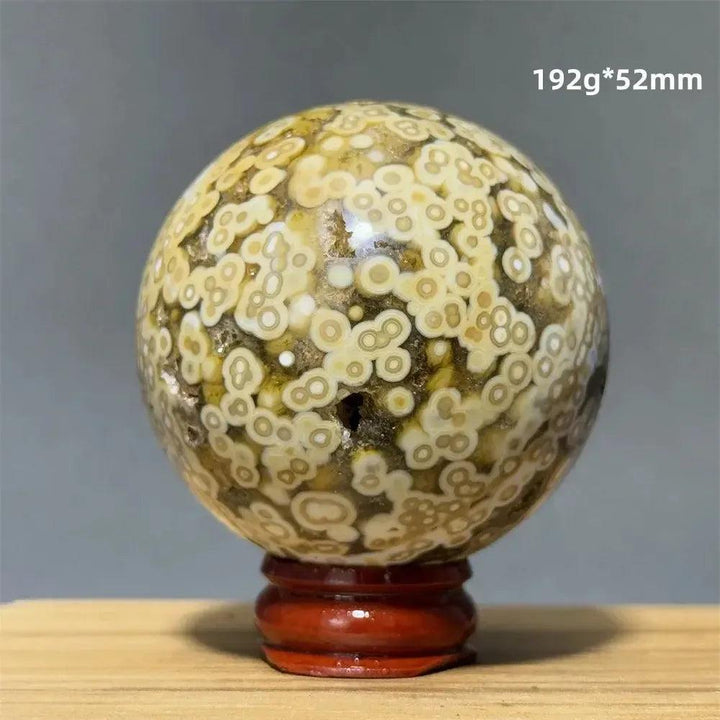 Ocean Jasper sphere with unique orbicular patterns in green, white, cream, pink, and red, on a red wooden base.