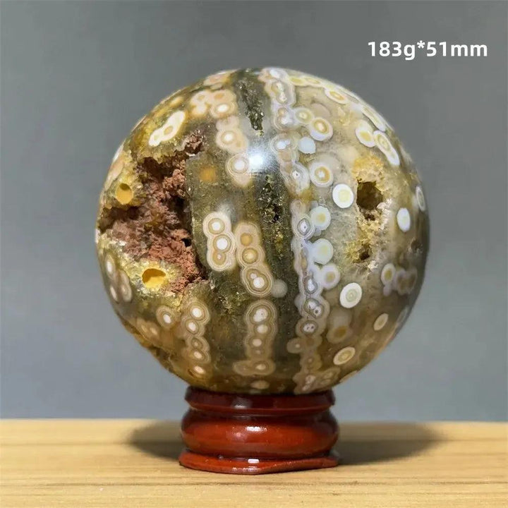 Ocean Jasper sphere from Crystal Destiny, with green, white, cream, pink, and red orbicular patterns on a wooden base.