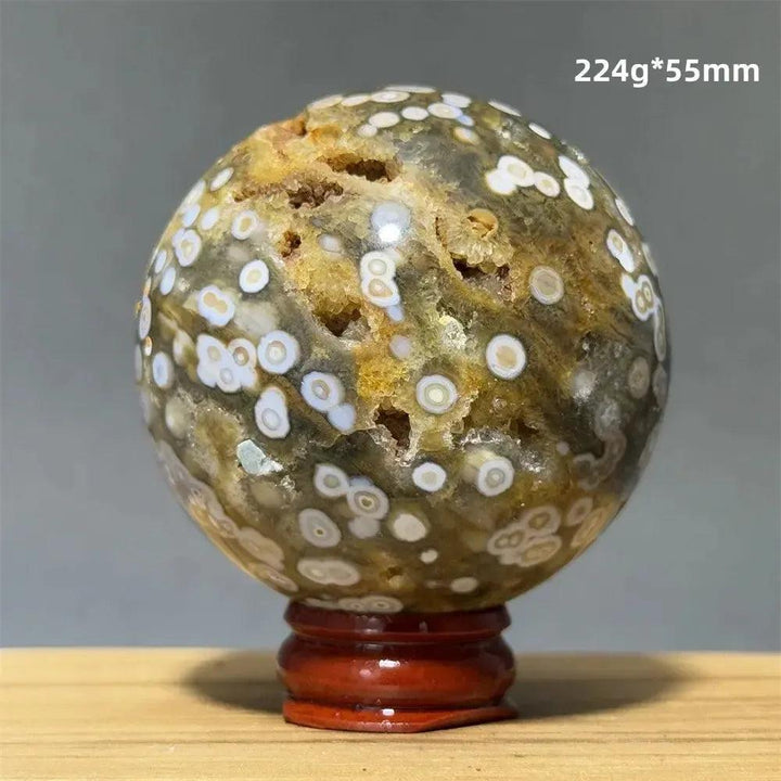 Ocean Jasper sphere with green, white, cream, pink, and red orbicular patterns on a wooden display base.