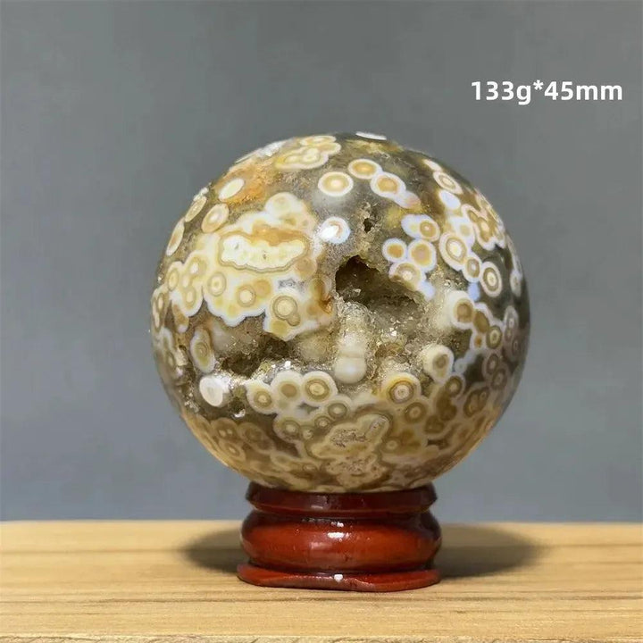 Ocean Jasper sphere with orbicular patterns in green, white, cream, pink, and red on a wooden base.