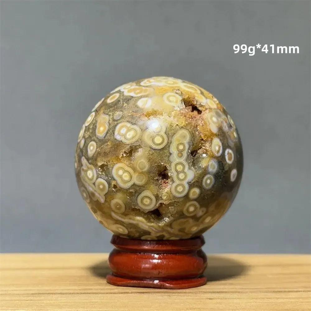 Ocean Jasper sphere by Crystal Destiny, with unique green, white, cream, pink, and red orbicular patterns on a wooden base.