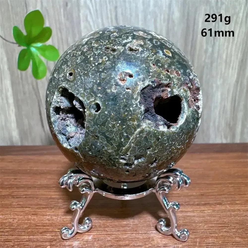 Unique Ocean Jasper sphere from Crystal Destiny, featuring deep green, brown, and white orbicular patterns with natural vugs, on a silver stand.