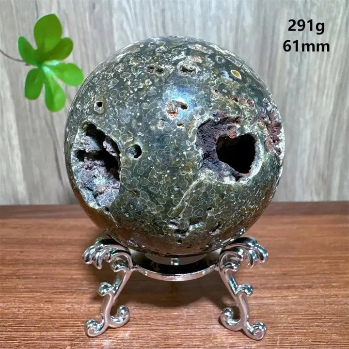Unique Ocean Jasper sphere from Crystal Destiny, featuring deep green, brown, and white orbicular patterns with natural vugs, on a silver stand.