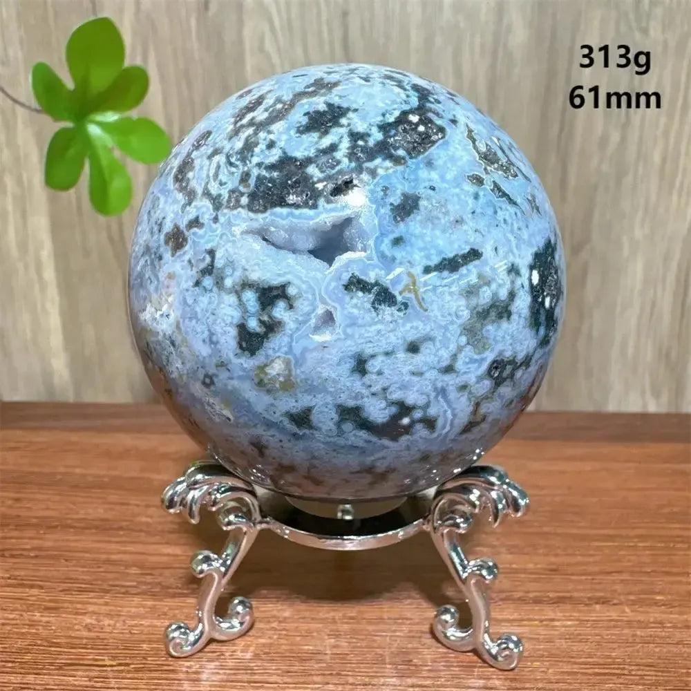 Ocean Jasper sphere from Crystal Destiny, featuring blue, green, and white orbicular patterns on a silver stand.