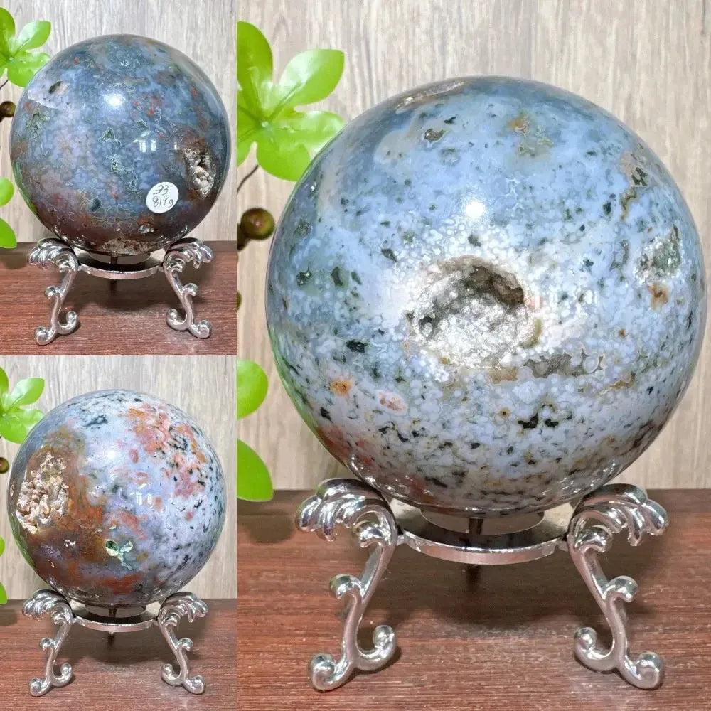 Ocean Jasper sphere from Crystal Destiny, displaying unique blue, green, and brown orbicular patterns with a geode cavity, on a silver stand.