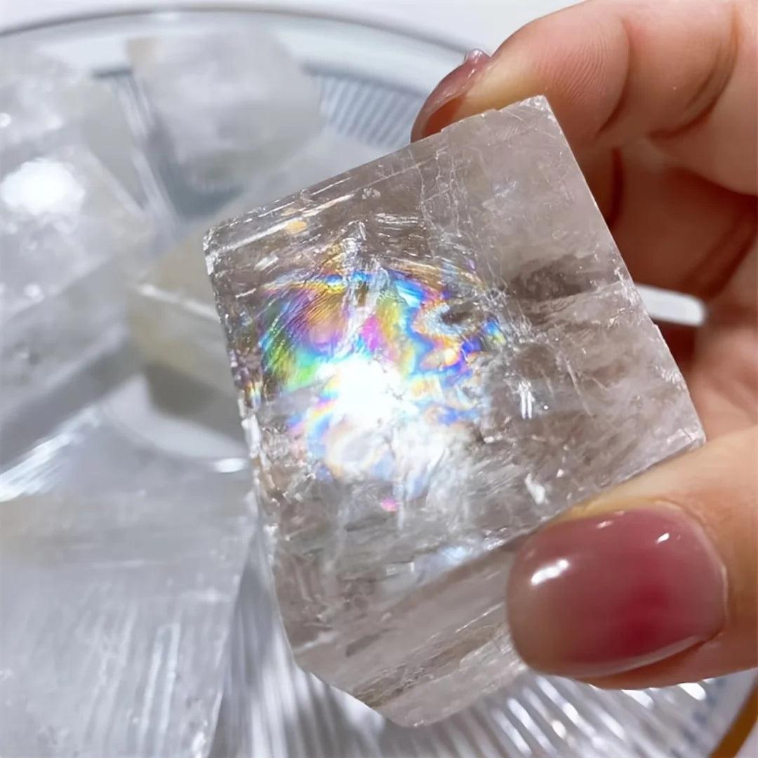 Hand holding a clear Brazilian optical calcite cube with a vibrant rainbow internal reflection, ideal for home decor.