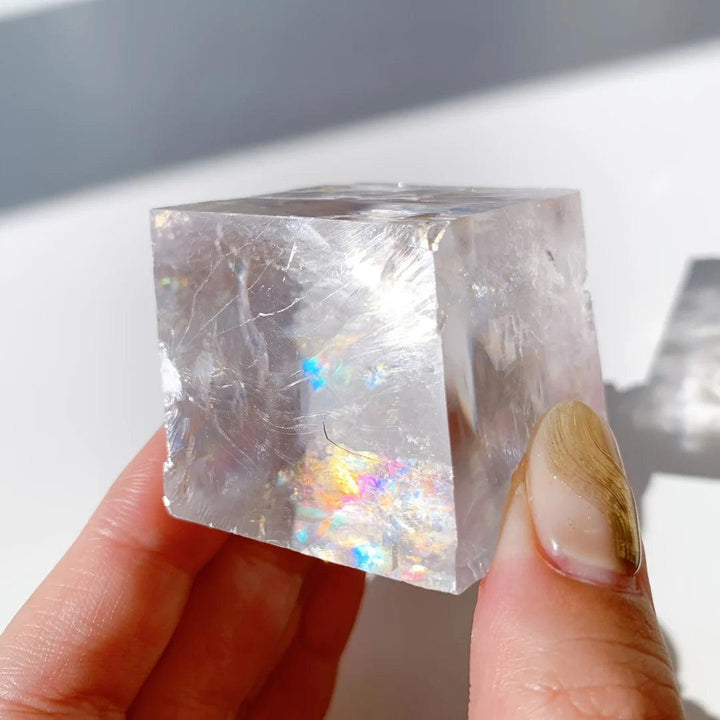 Clear Brazilian Optical Calcite cube held in hand, showing iridescent rainbow reflections.