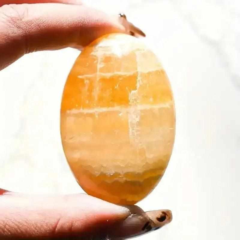 Smooth, glowing orange calcite palm stone held in hand, featuring warm, polished natural stone for sacral chakra energy.