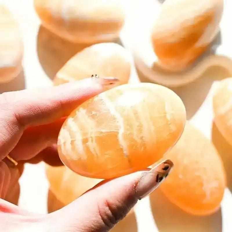 Hand holding a smooth, glowing orange calcite palm stone with natural white banding, perfect for sacral chakra energy.