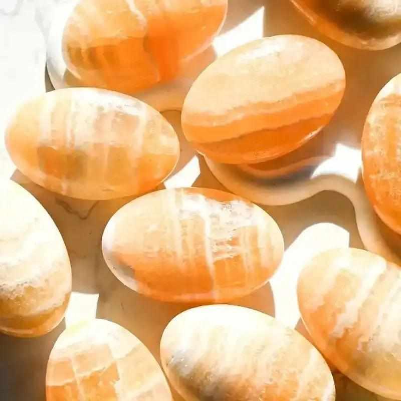 Polished orange calcite palm stones with glowing, warm hues, perfect for sacral chakra energy and creative inspiration.