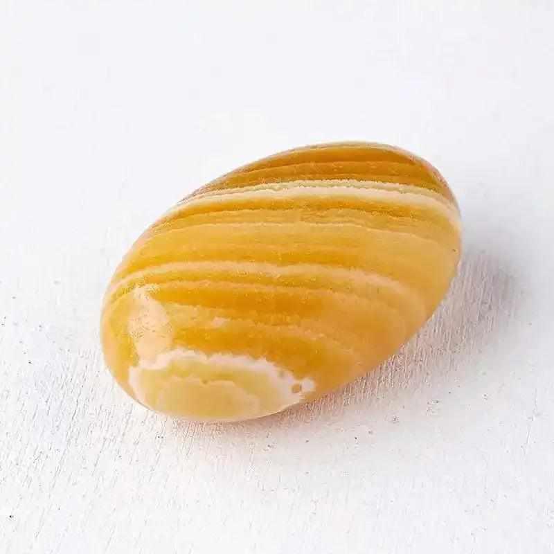 Smooth, glowing orange calcite palm stone with natural banding, polished for sacral chakra energy and creative focus.