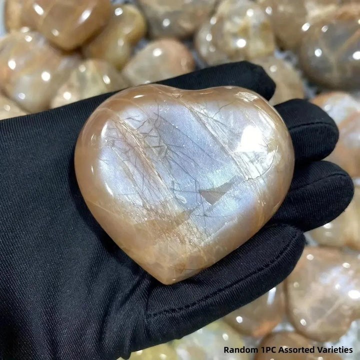 Hand-carved peachy-orange Orange Moonstone heart with iridescent shimmer, held by Crystal Destiny.
