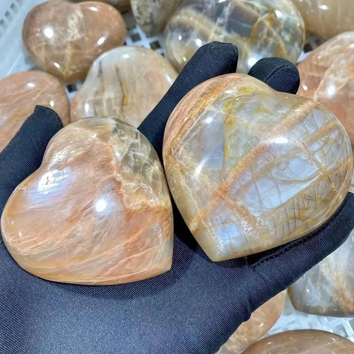 Two hand-carved Orange Moonstone hearts from Crystal Destiny, glowing with peachy-orange tones and iridescent shimmer.