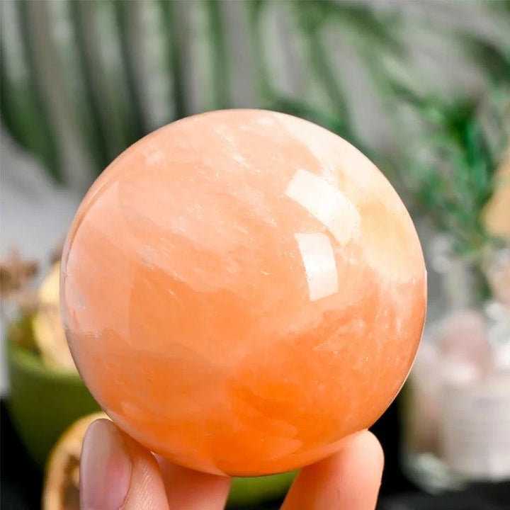 Polished orange selenite crystal sphere with a warm, translucent peach glow for healing and radiant energy.