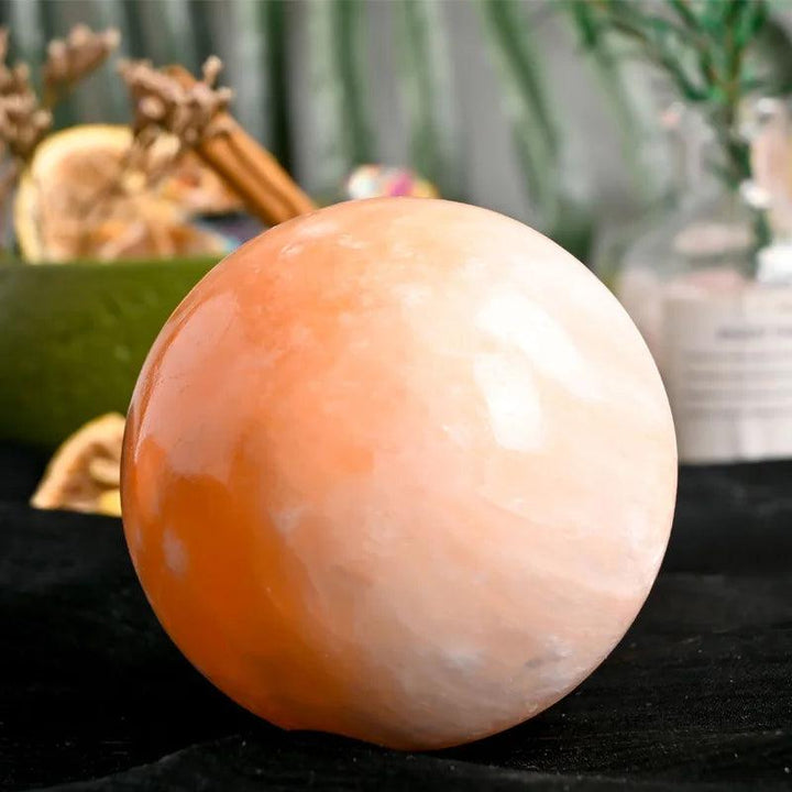 Polished orange selenite sphere with warm peach tones, radiating calming energy and light for healing and meditation.