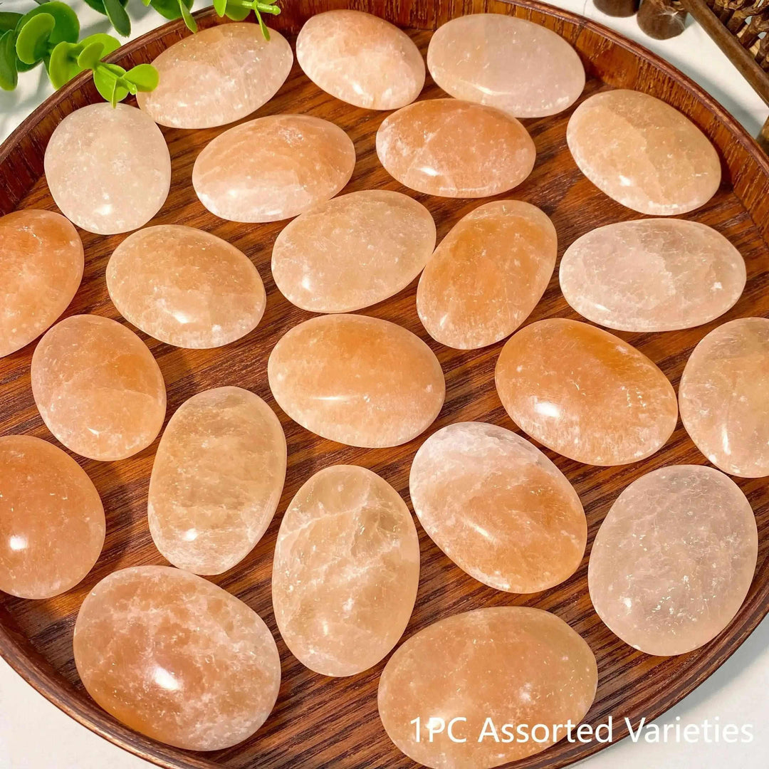 Smooth, polished Orange Selenite palm stones with a silky, glowing finish in warm peach tones for chakra balancing.