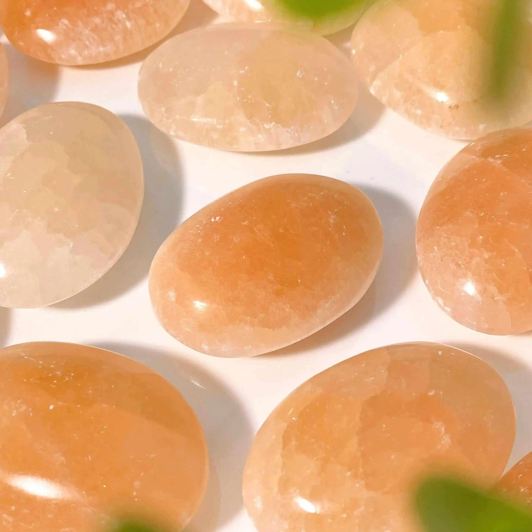 Smooth, polished orange selenite palm stones with a silky, glowing finish in warm peach tones for chakra balancing.
