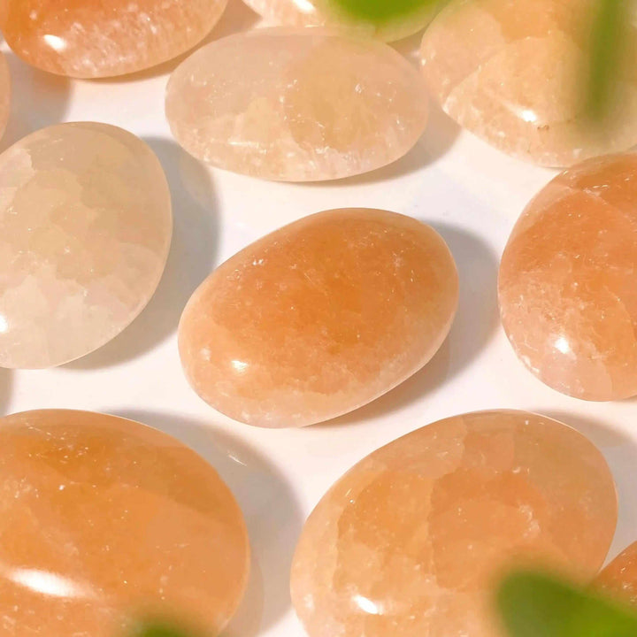 Smooth, polished orange selenite palm stones with a silky, glowing finish in warm peach tones for chakra balancing.