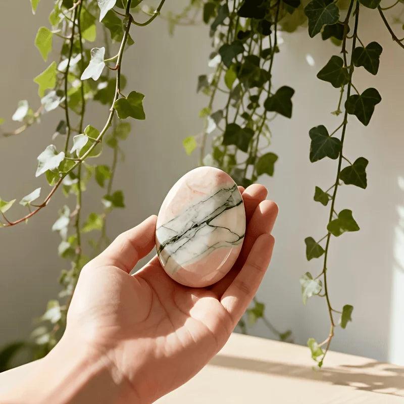Polished pink and green sunstone palm stone held in hand for vitalizing solar energy.