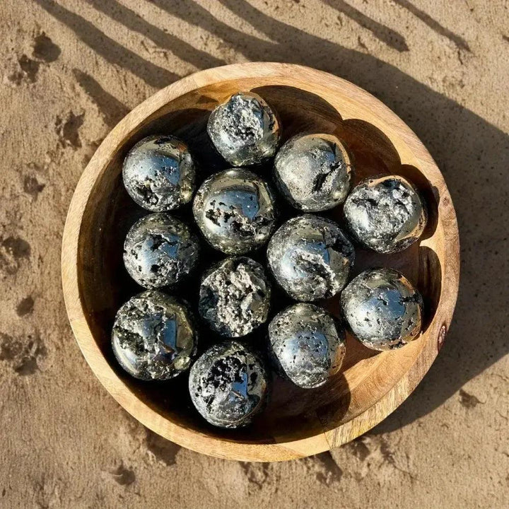 Peruvian Pyrite Crystal Ball: A wooden bowl filled with twelve metallic gold, raw pyrite spheres, shimmering with abundance.
