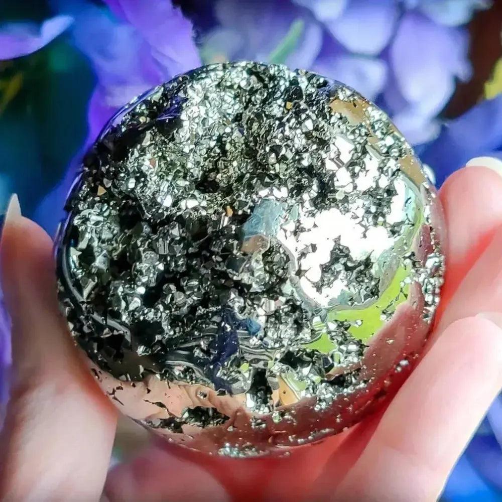 Peruvian Pyrite Crystal Ball: Polished metallic gold sphere with sparkling cubic pyrite inclusions, held in a hand.