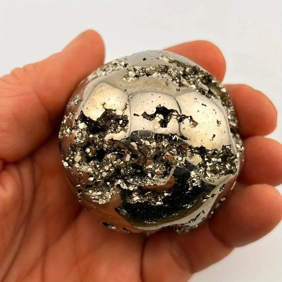 Peruvian Pyrite Crystal Ball: Polished metallic gold sphere with sparkling cubic crystal inclusions, held in a hand.