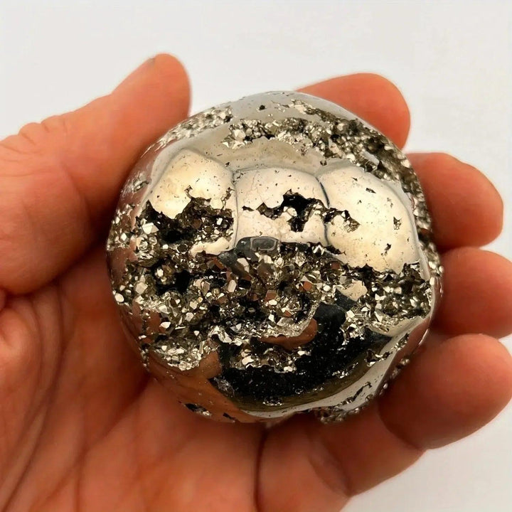 Peruvian Pyrite Crystal Ball: Polished metallic gold sphere with sparkling cubic crystal inclusions, held in a hand.