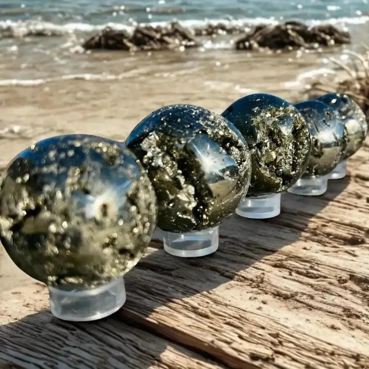 Peruvian Pyrite Crystal Ball: Five metallic gold spheres with cubic crystal inclusions on a wooden surface by the ocean.