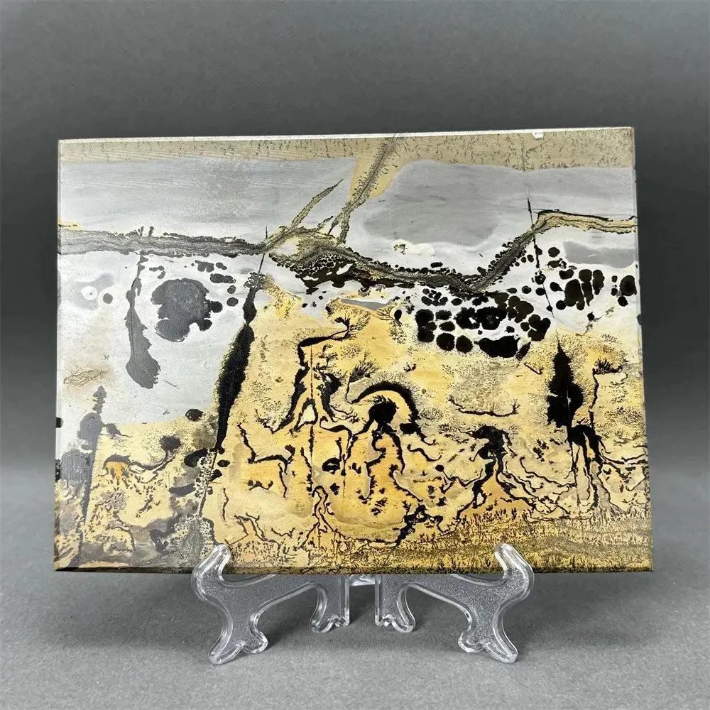 Polished Picture Jasper slice with unique landscape patterns in ochre, brown, and grey on a clear stand from Crystal Destiny.
