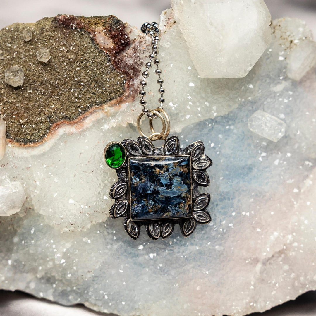 Pietersite 925 Sterling Silver Pendant with swirling blues, golds, and browns, accented by a vibrant green gemstone.