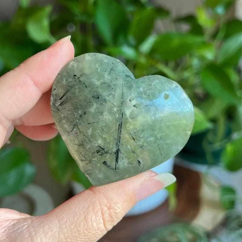 Polished apple green Prehnite heart crystal with natural black inclusions, perfect for calming meditation and healing.