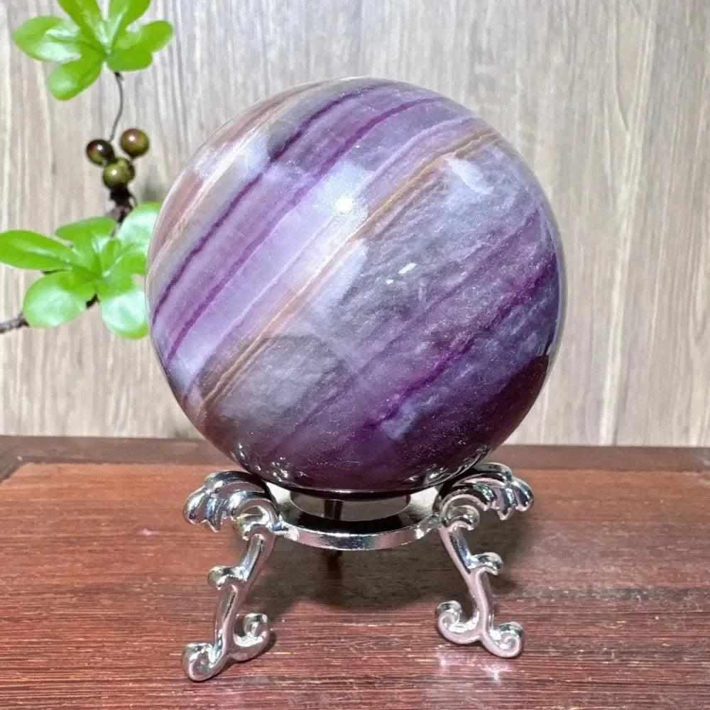 Polished purple fluorite crystal sphere with deep violet banding, displayed on an ornate silver stand for third eye clarity.