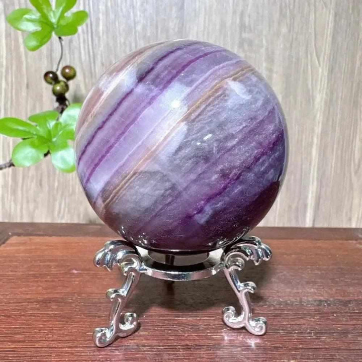 Polished purple fluorite crystal sphere with deep violet banding, displayed on an ornate silver stand for third eye clarity.