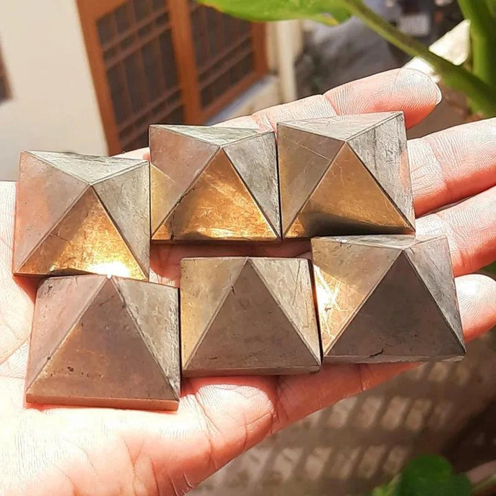 Six metallic, mirror-bright Pyrite Crystal Pyramids for manifestation and abundance, held in a hand.