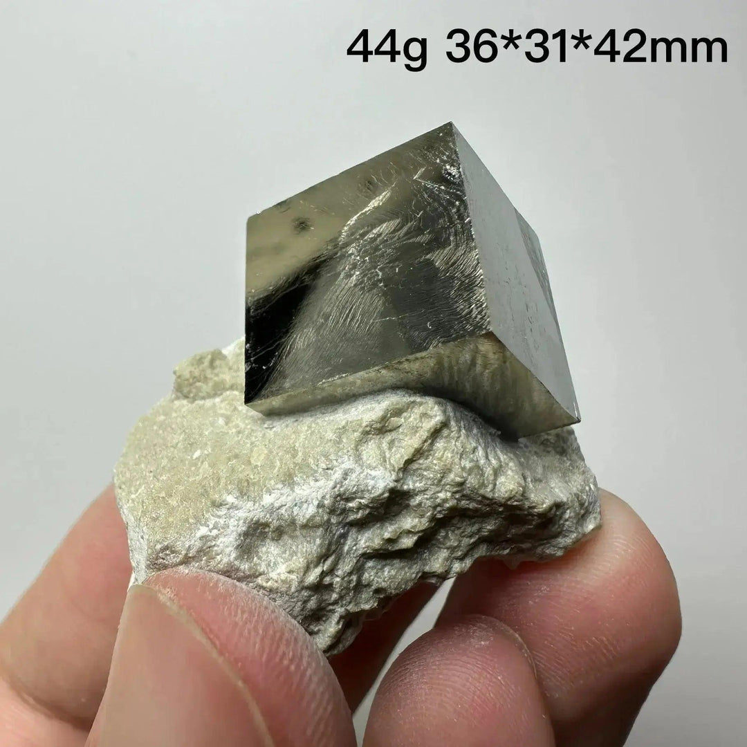 Metallic gold Pyrite Cube Crystal Specimen from Crystal Destiny, naturally formed on a light matrix, held by fingers.