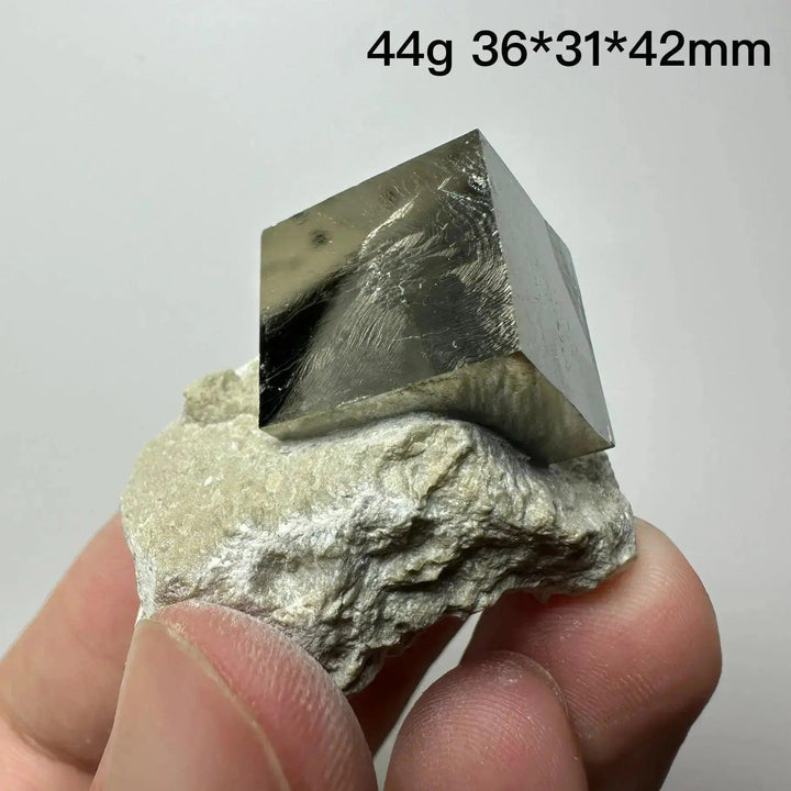 Metallic gold Pyrite Cube Crystal Specimen from Crystal Destiny, naturally formed on a light matrix, held by fingers.