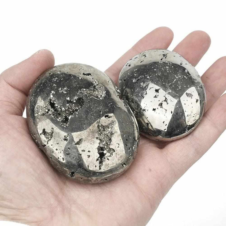 Two polished Pyrite palm stones with a bright golden metallic luster, held in a hand for confidence and abundance.