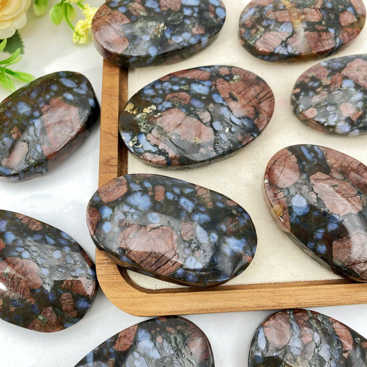 Polished Que Sera stone oval palm stones with natural blue, pink, and black speckled patterns.