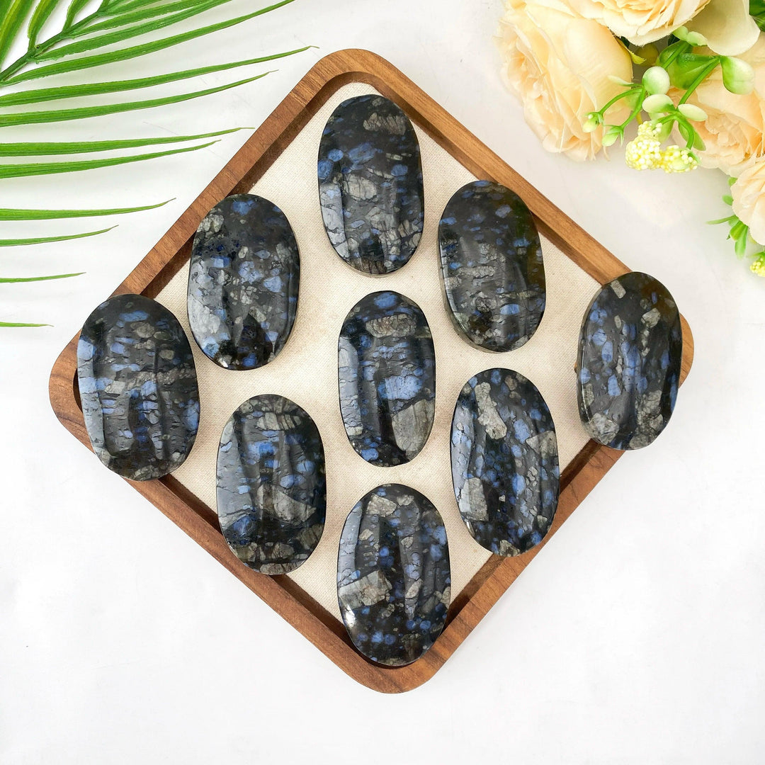Polished Que Sera stone oval palm stones with blue and grey flecks on a wooden tray.