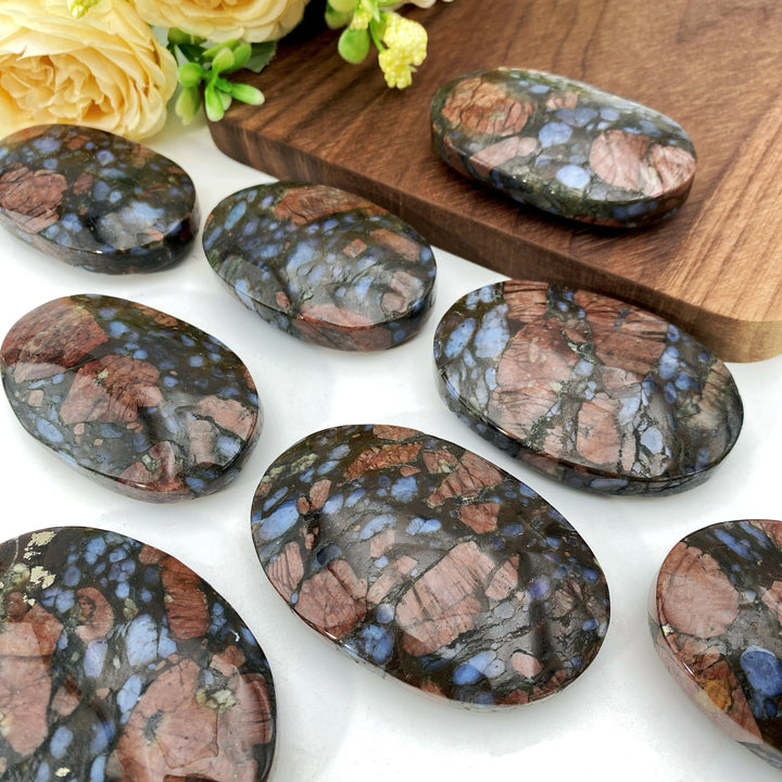 Polished Que Sera palm stones with unique blue and brown speckled patterns for healing and decor.