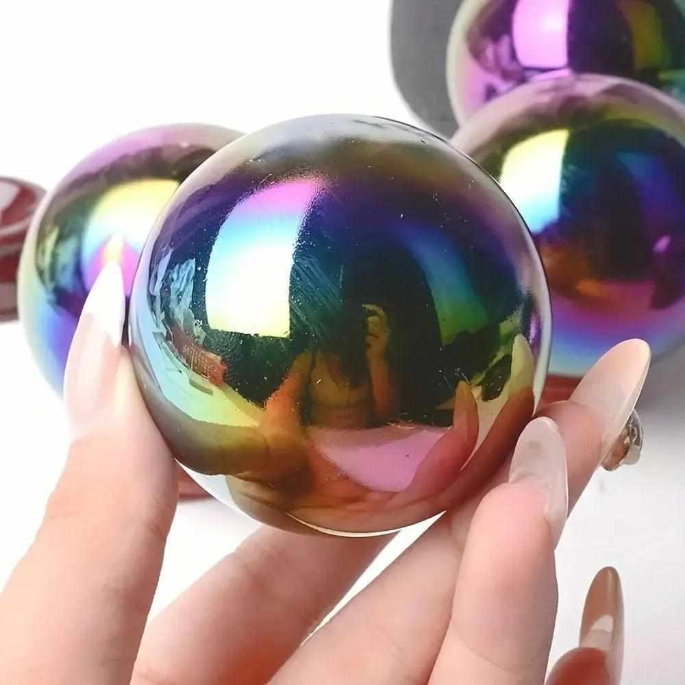 Hand holding a Rainbow Aura Obsidian crystal sphere with iridescent violet, gold, and teal flashes for grounding energy.