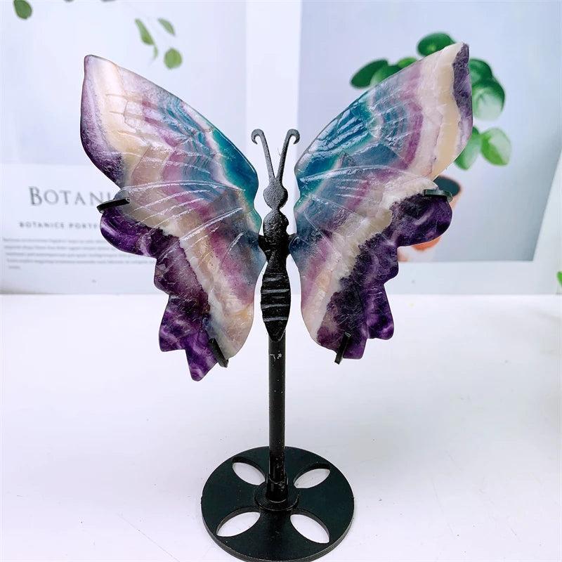 Rainbow fluorite crystal butterfly wings carving, displaying vibrant purple, green, and clear bands on a black stand.