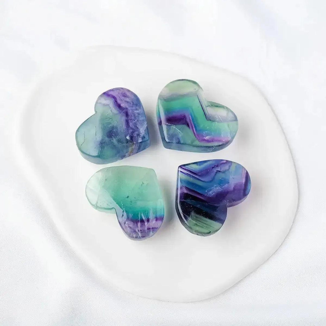 Four polished Rainbow Fluorite crystal hearts from Crystal Destiny, showcasing vibrant purple, green, and blue bands.