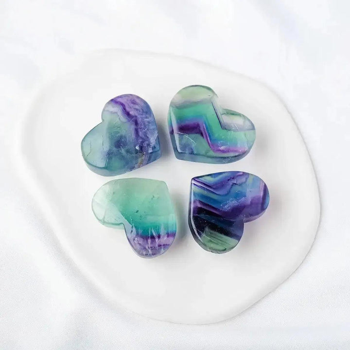 Four polished Rainbow Fluorite crystal hearts from Crystal Destiny, showcasing vibrant purple, green, and blue bands.